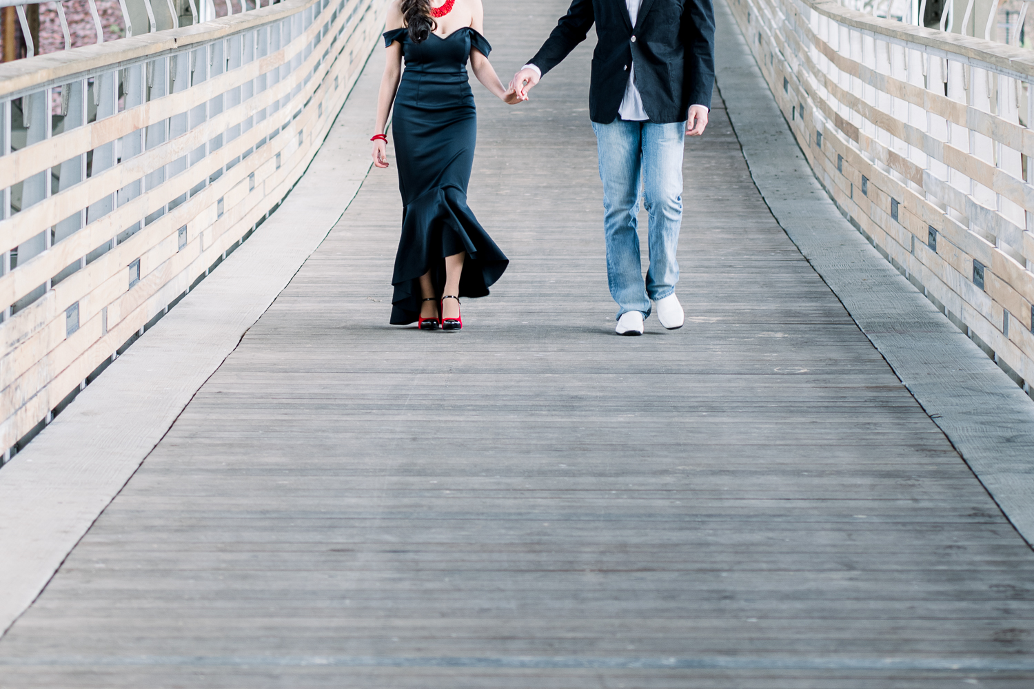 Engaged couple in matching black outfits walking along industrial bridge