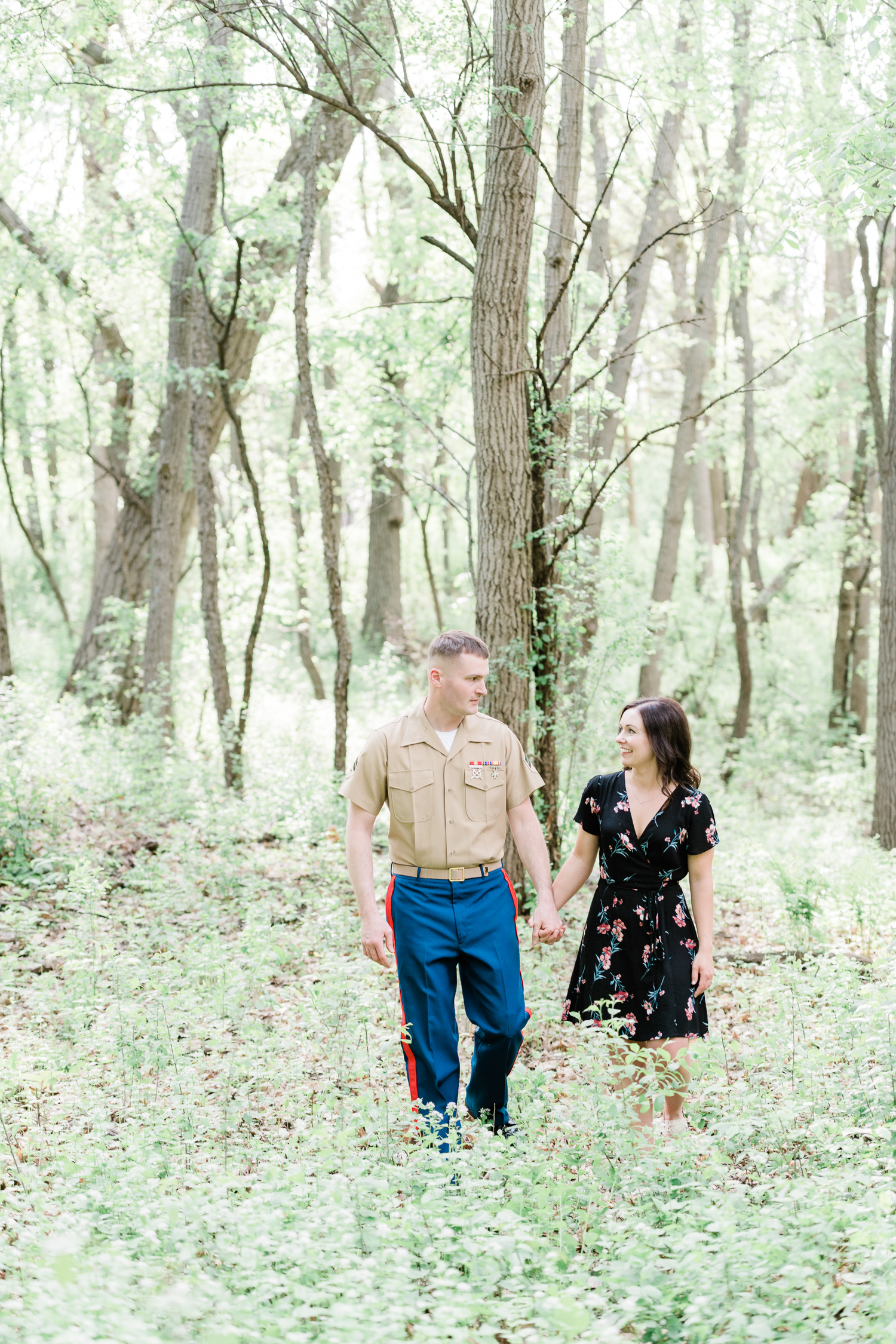 Girl in black floral dress and guy in military uniform hold hands while walking in the park
