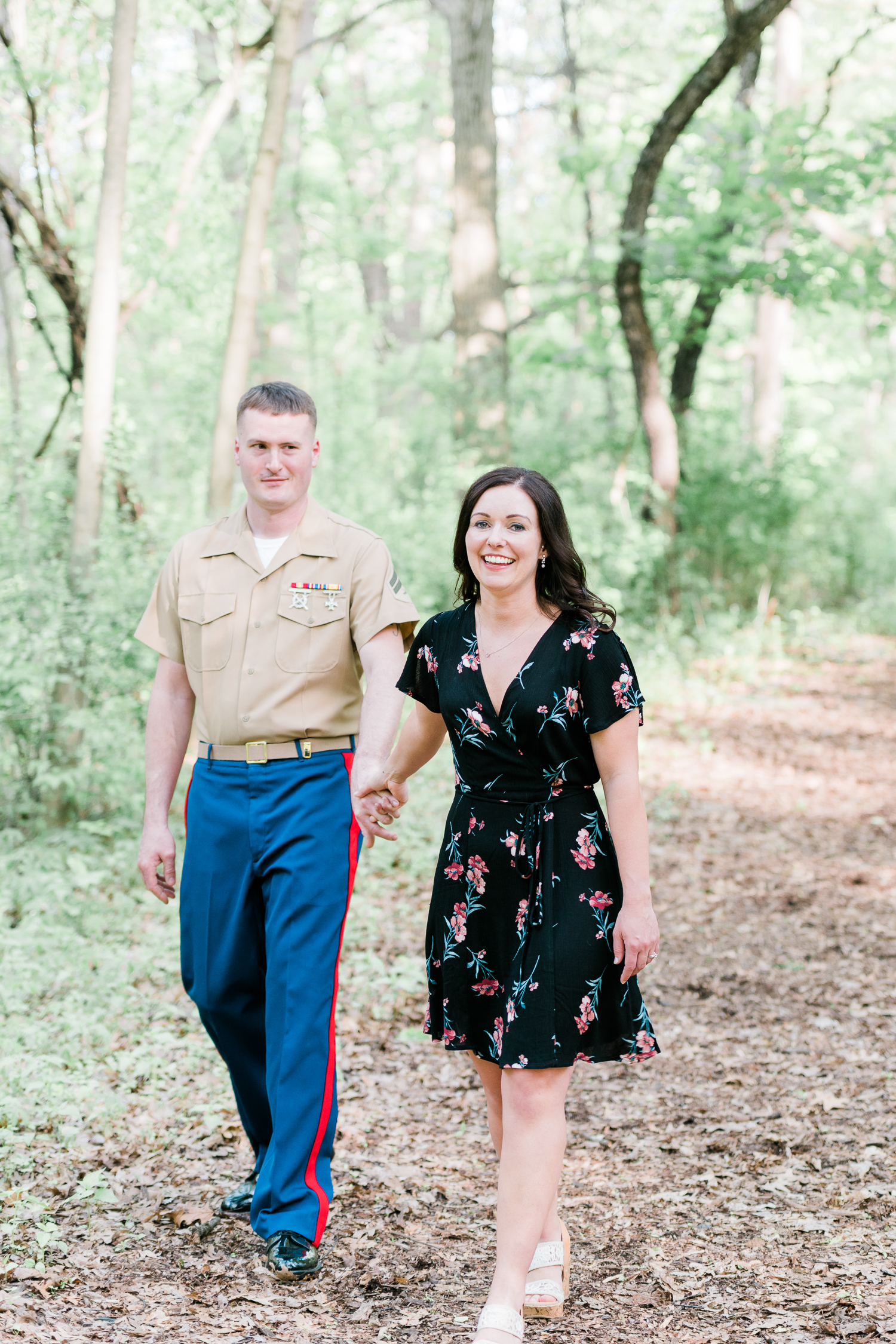 Girl in black floral dress and guy in military uniform hold hands while walking in the park
