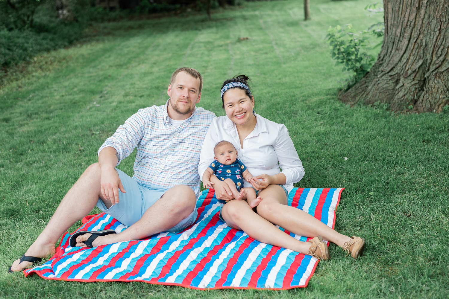 Family with newborn sitting on a picnic blanket on their backyard