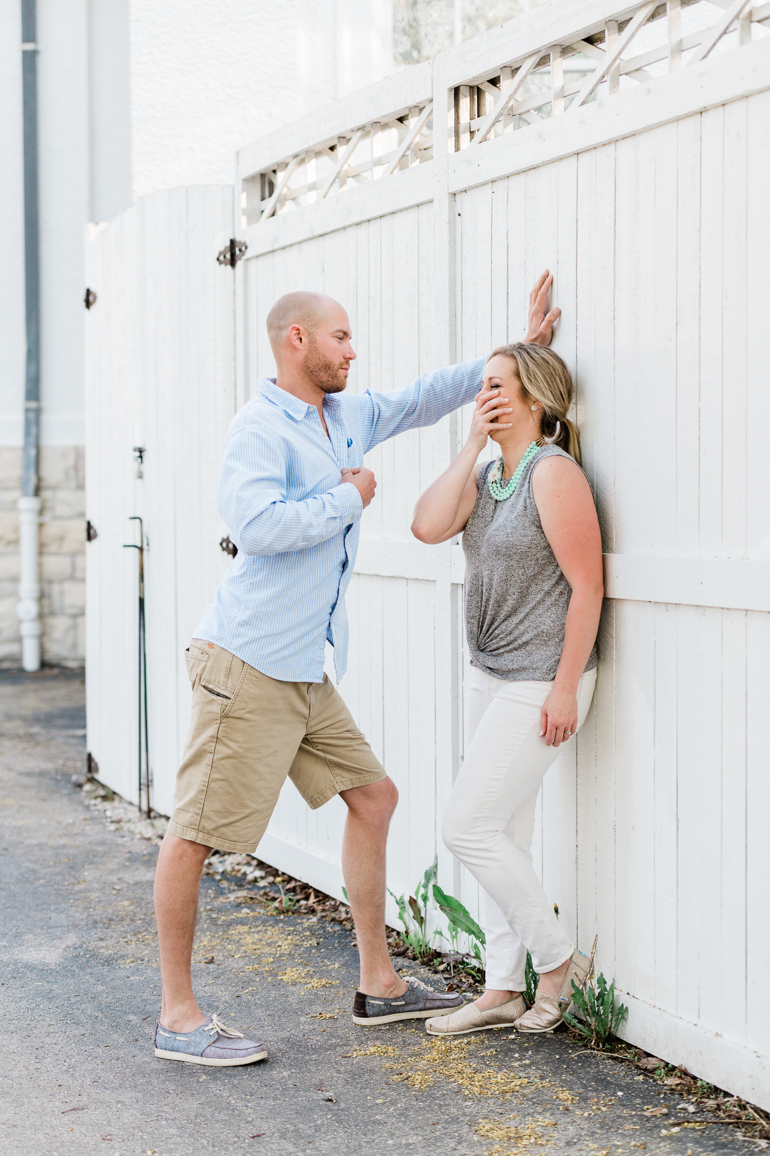 Fiance unbuttons light blue shirt in front of giggling fiance against a white wall