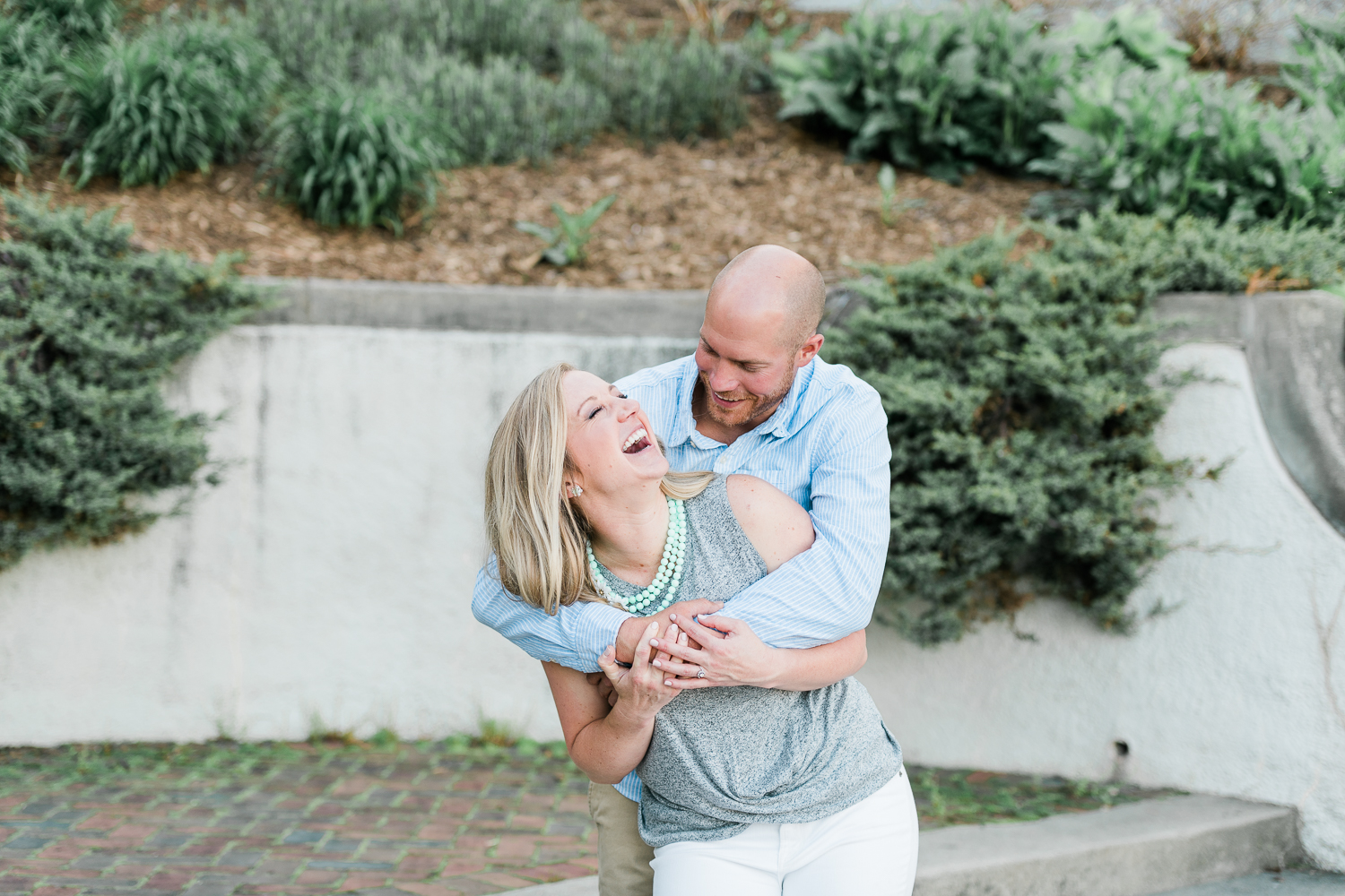 Engaged couple in gray and light blue hugging tightly while laughing