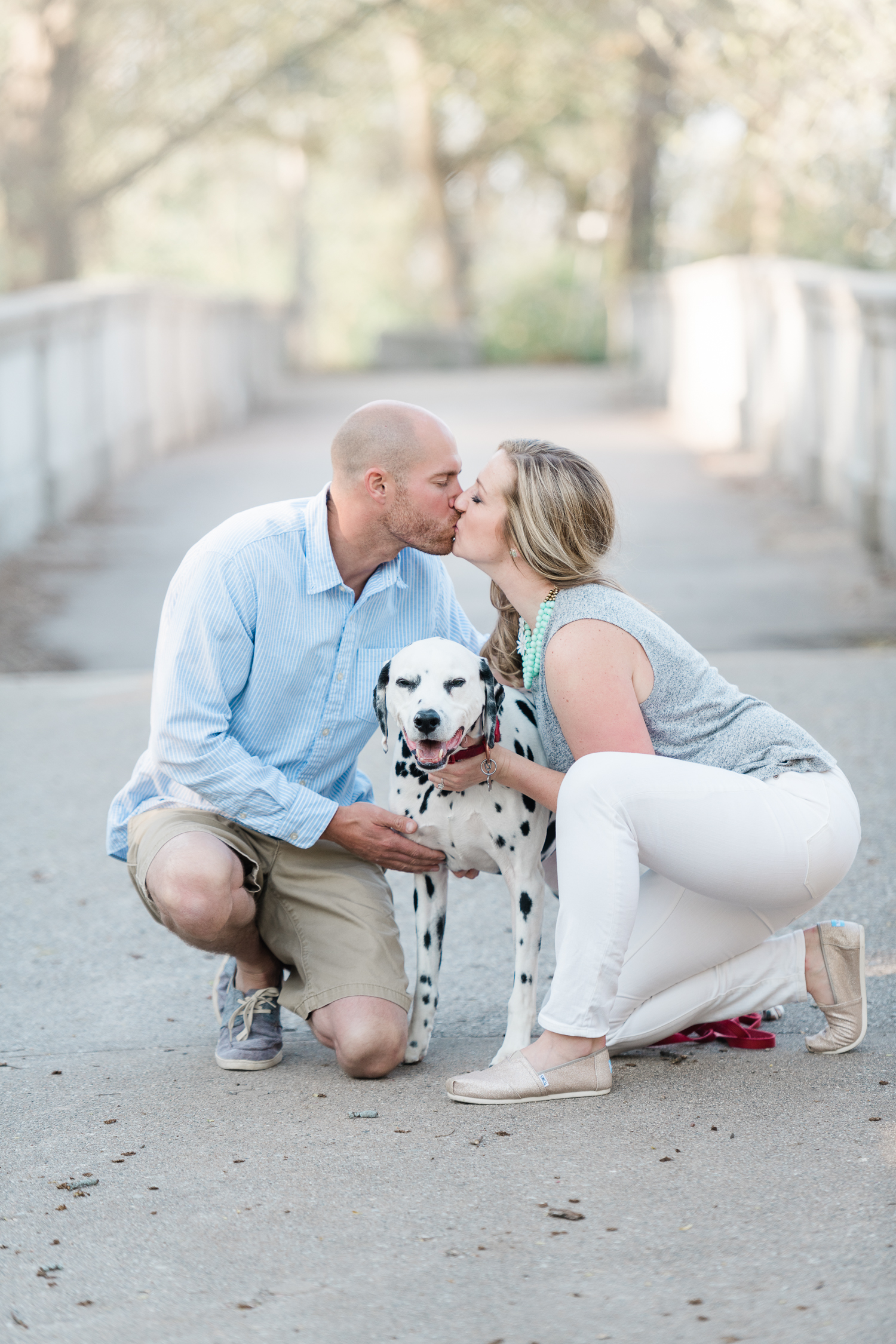 Engaged couple sits down ad kiss with their Dalmatian at Lake Park