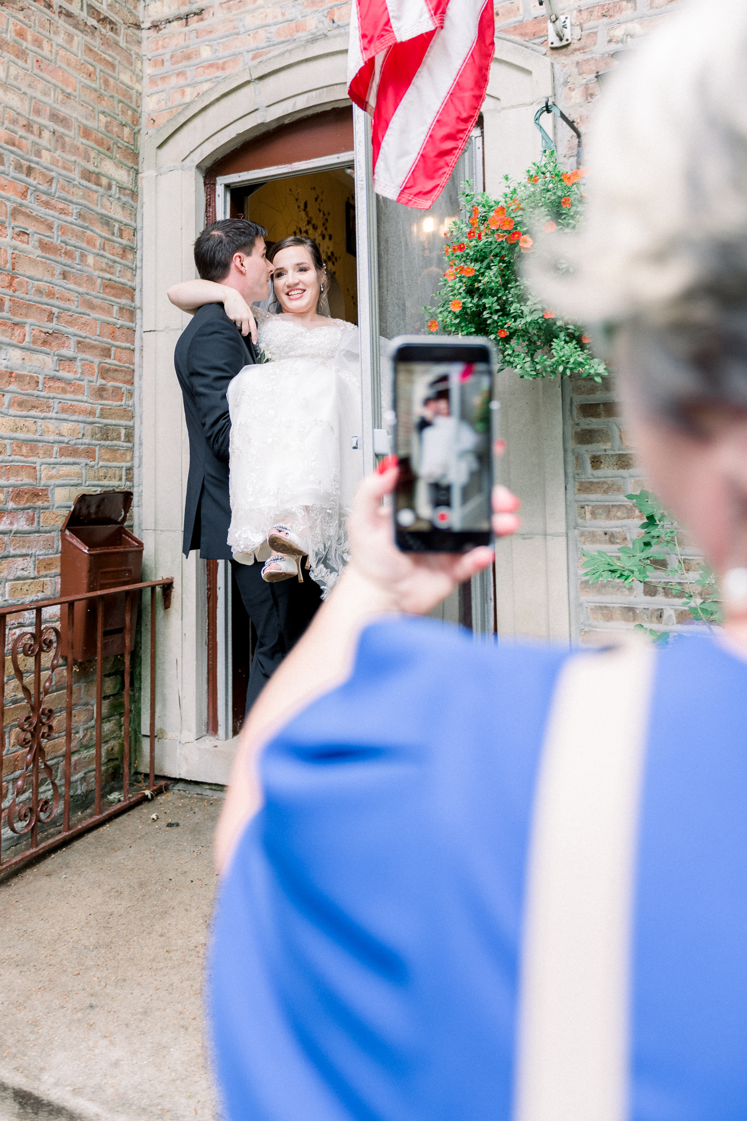 Groom carries bride inside her house and a lady with a cellphone is filming them