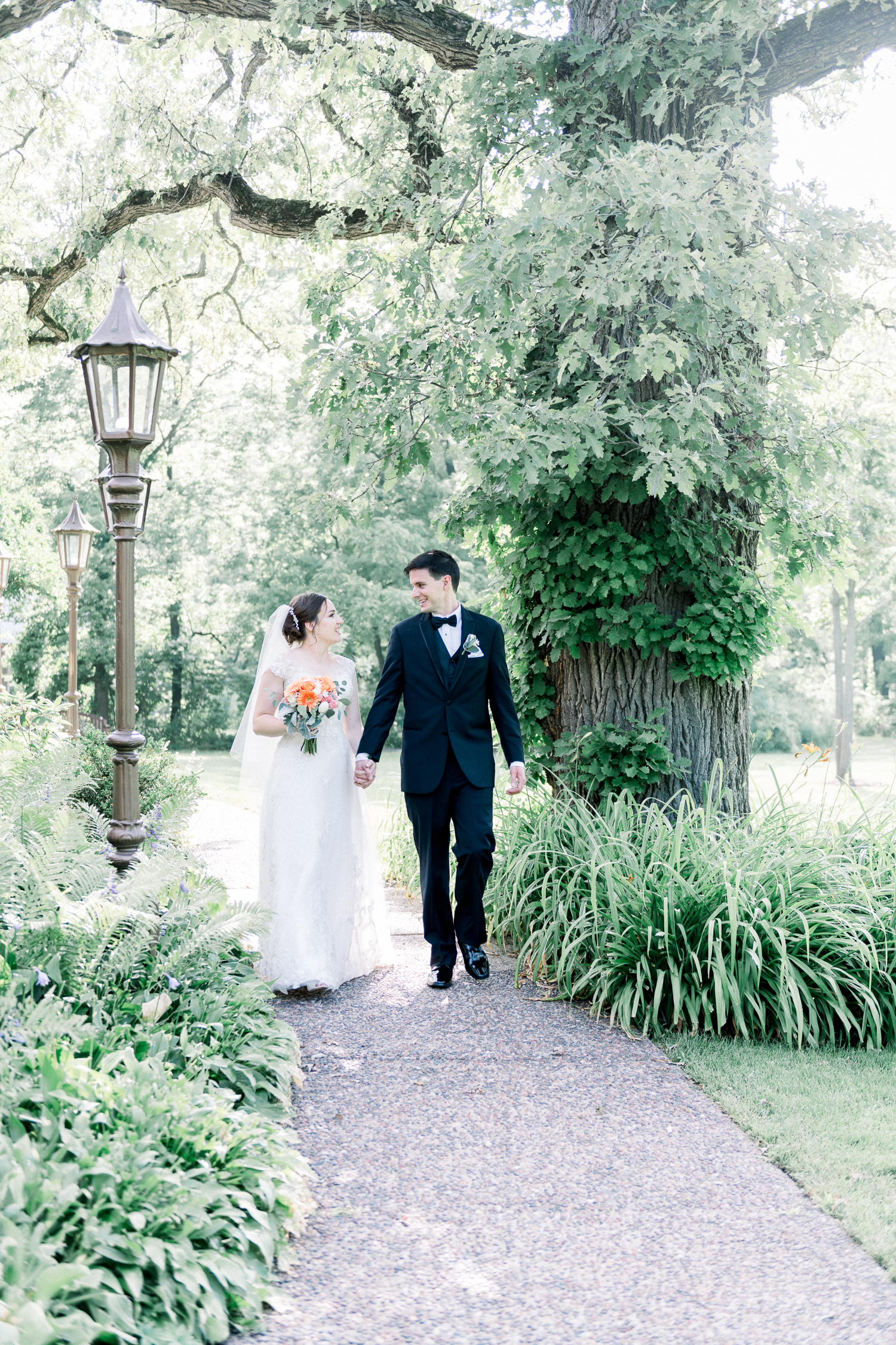Bride and groom walk along a path surrounded by greeneries