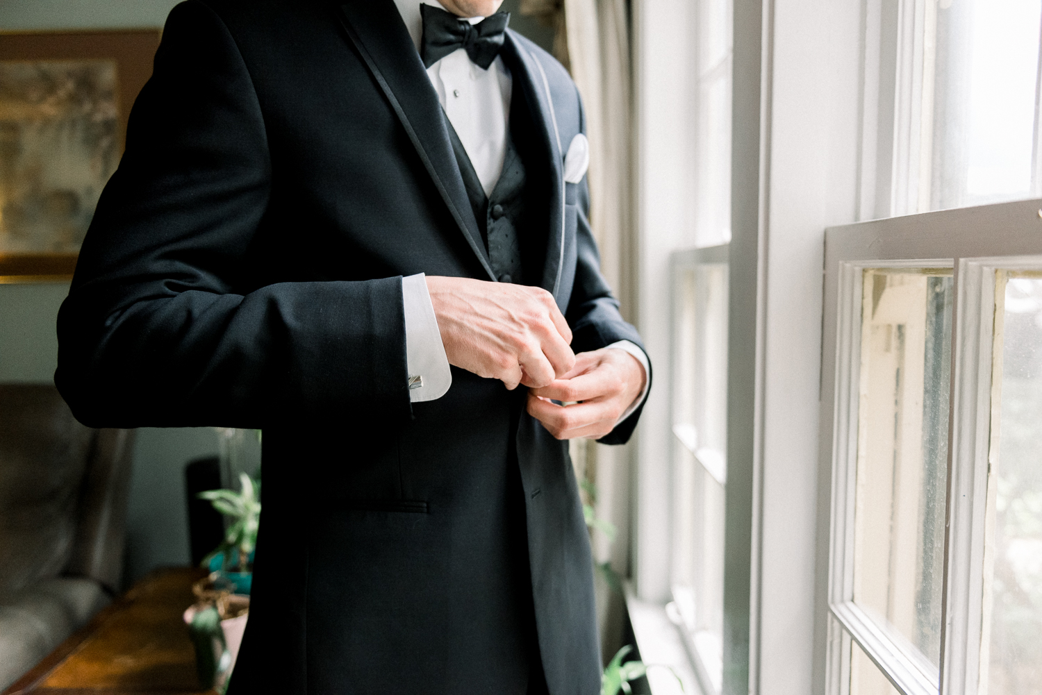 Close up of groom in black tuxedp buttoning the jacket