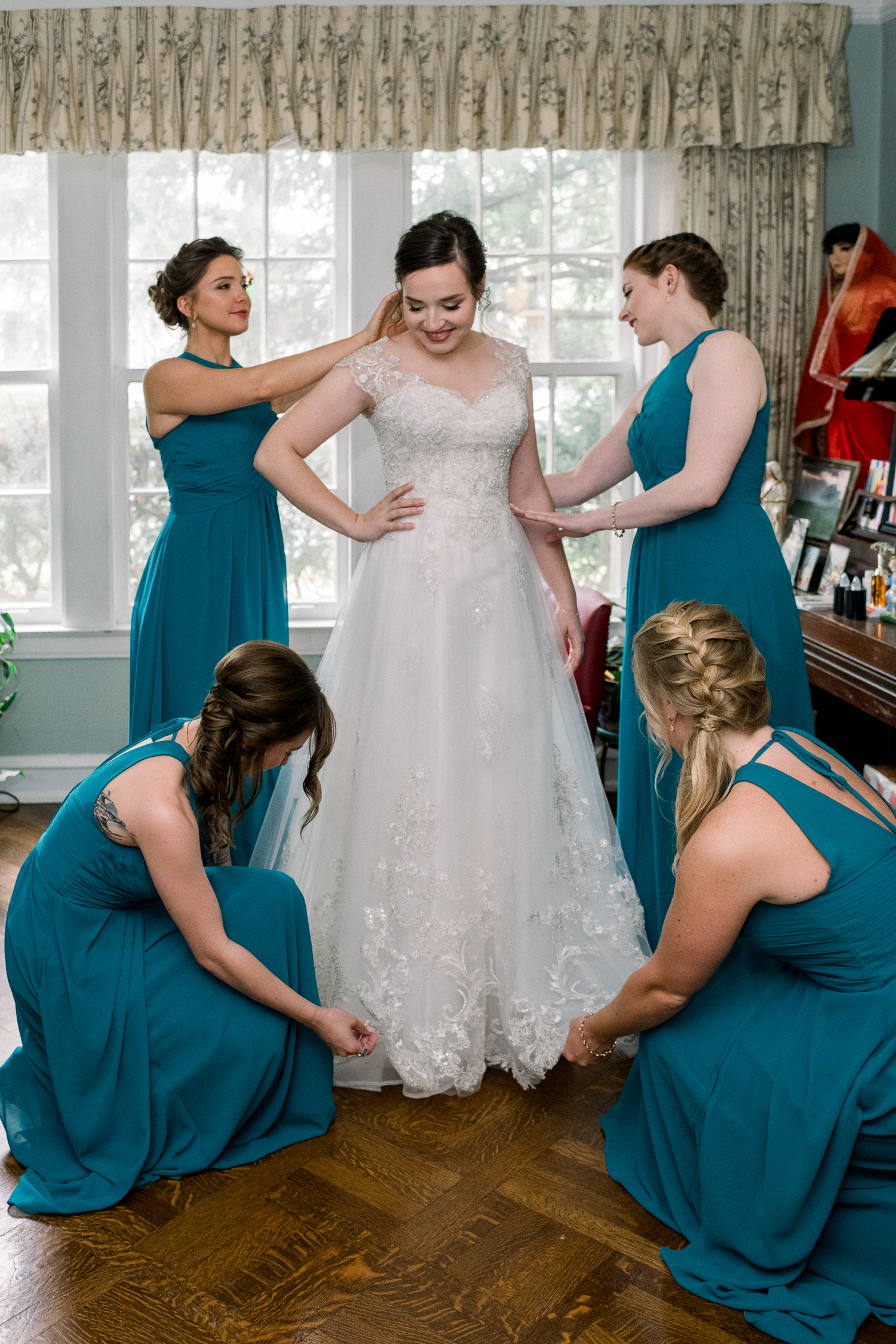 Bride's bridesmaids in teal dresses are helping her with her wedding dress