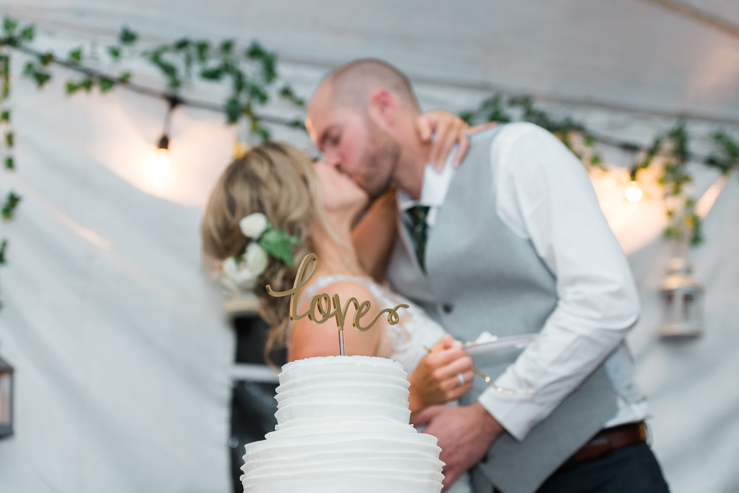 Newly married couple kissing with cake topper that states Love on the foreground