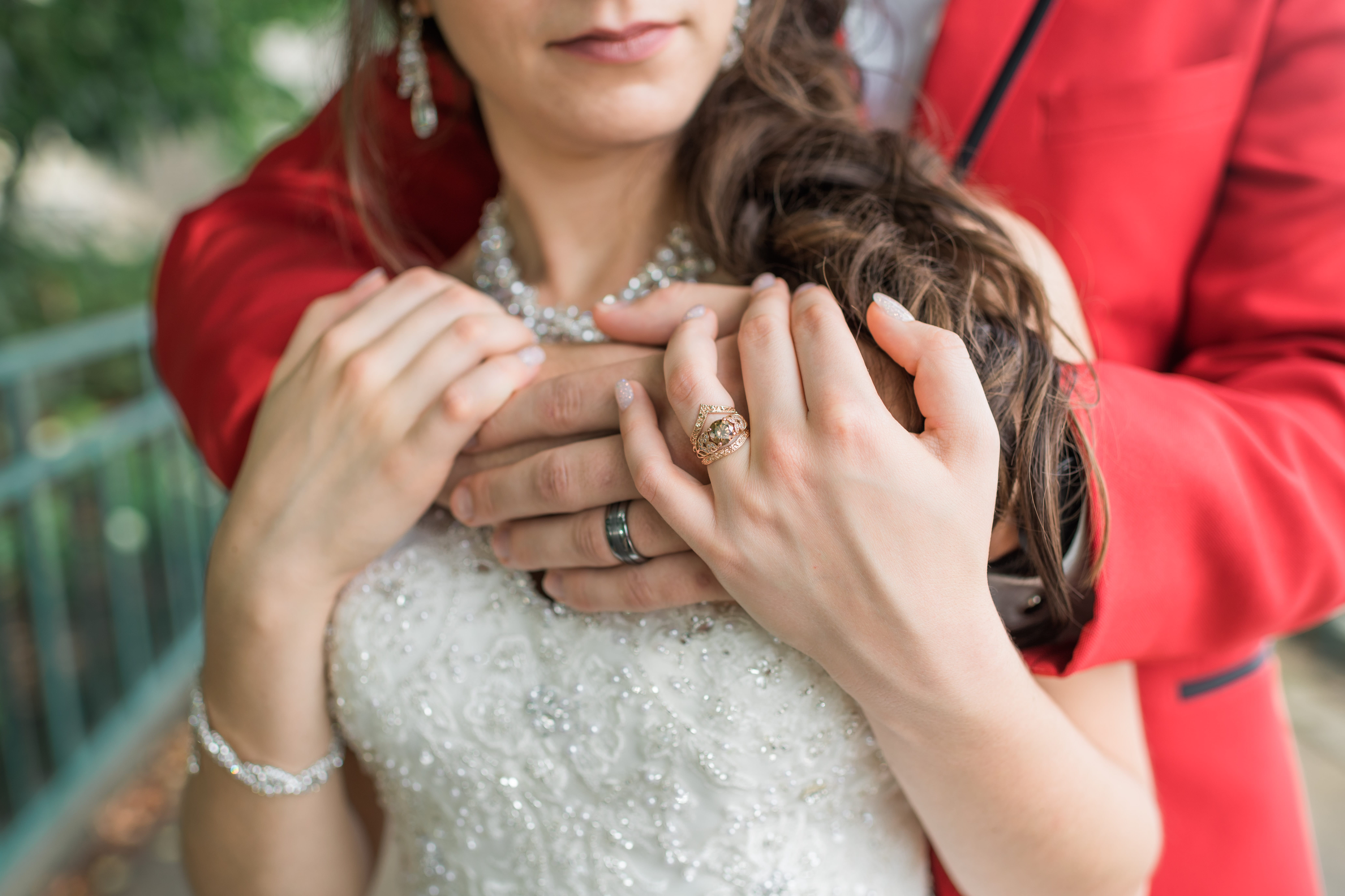 Bride holds onto grooms hands around her shoulders wearing their wedding bands
