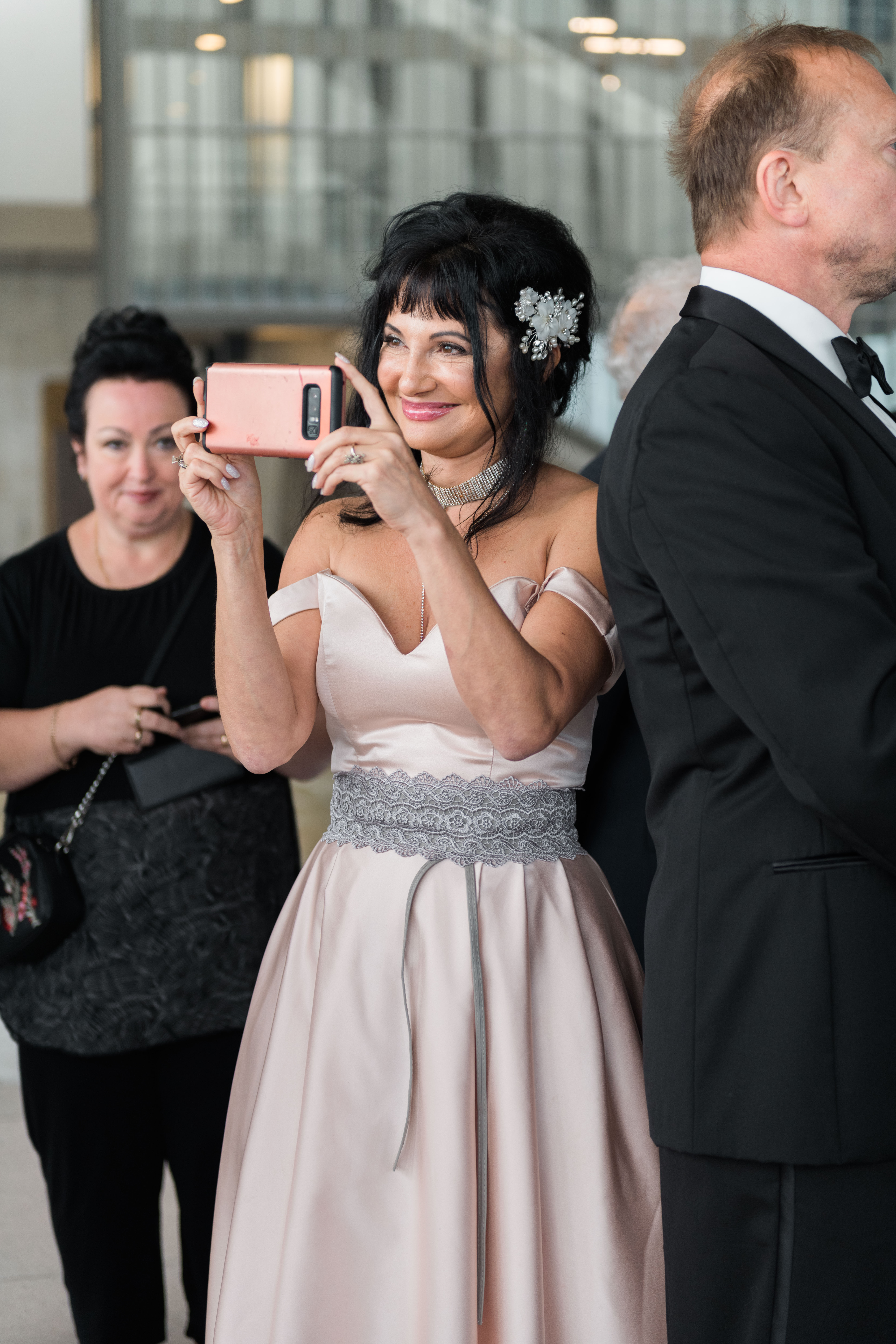 Smiling mother of the groom holding a cellphone while filming her son at the altar