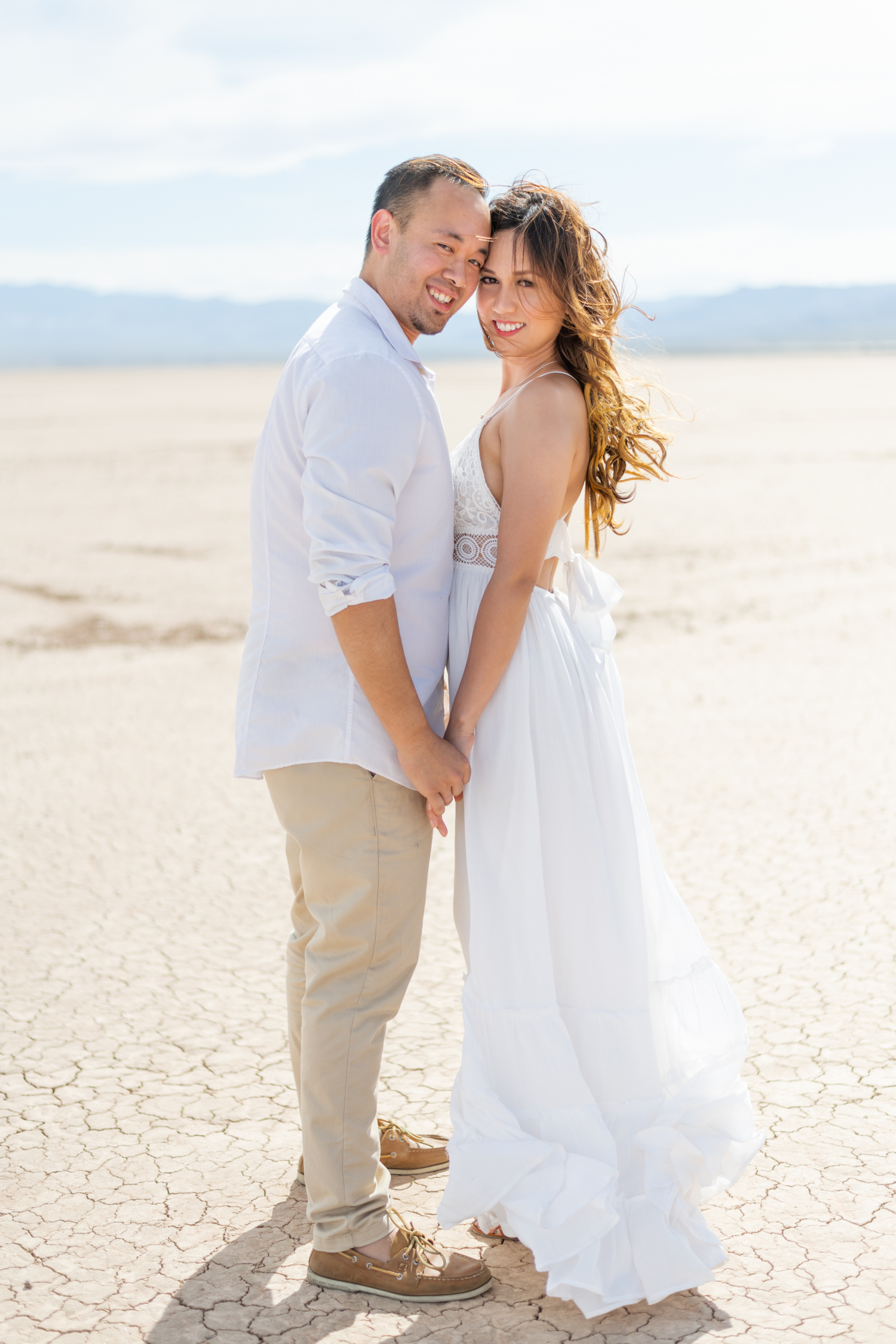 Couple in white outfits hold hands and forehead touching for Las Vegas engagement session