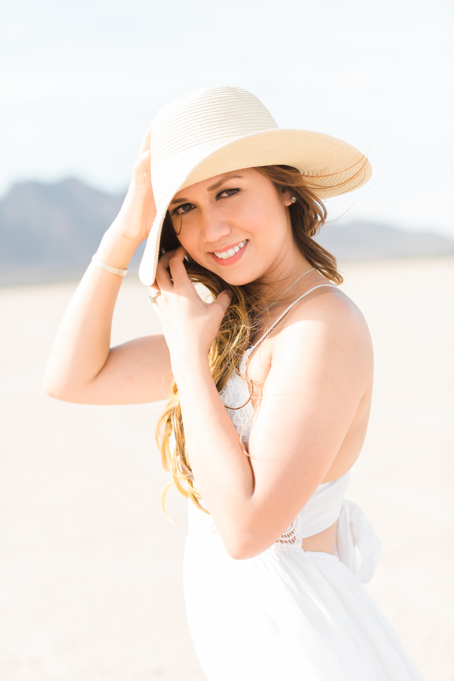 Girl on a white dress holds onto her hat as she smiles