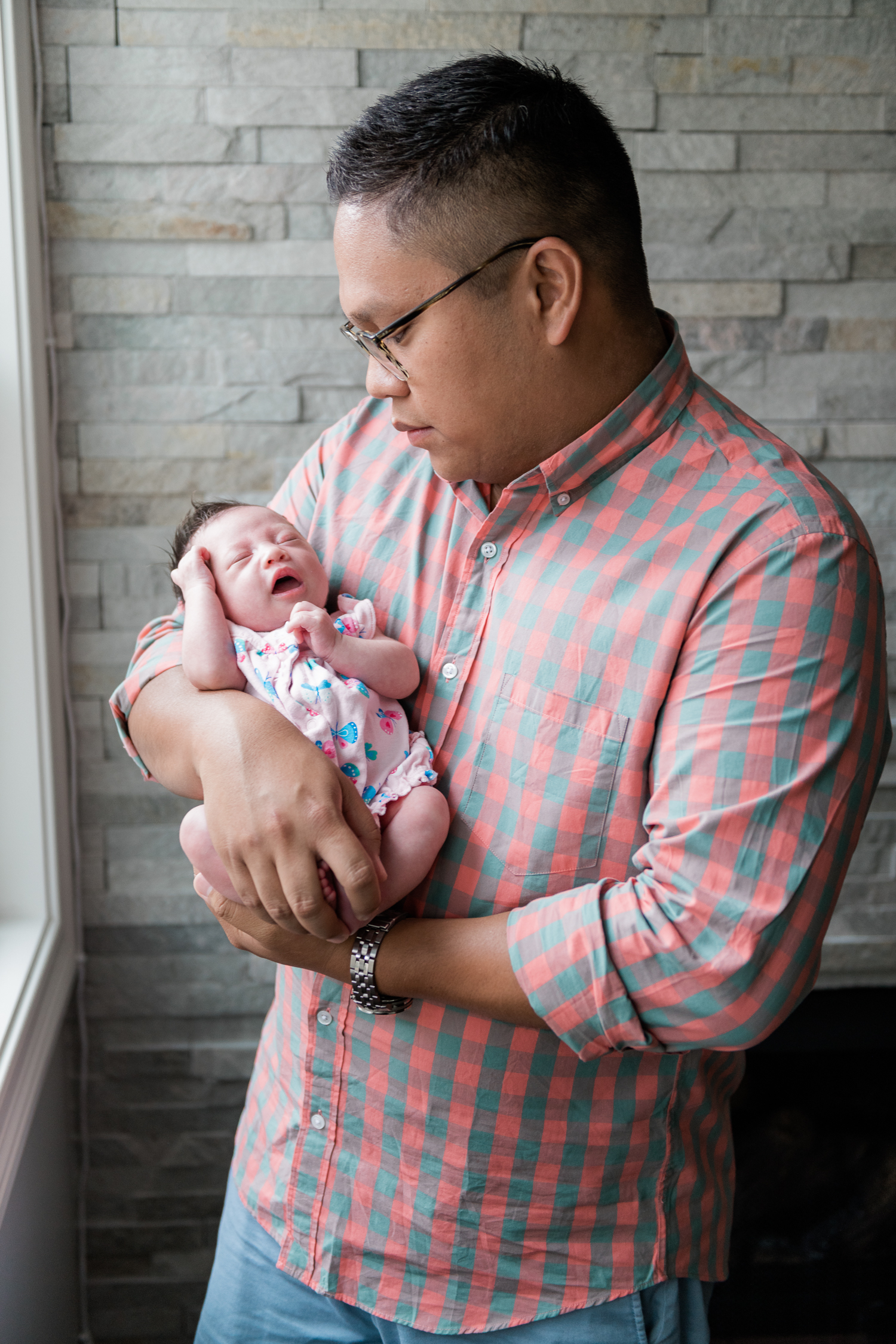 Father holds newborn baby girl in his arms by the window