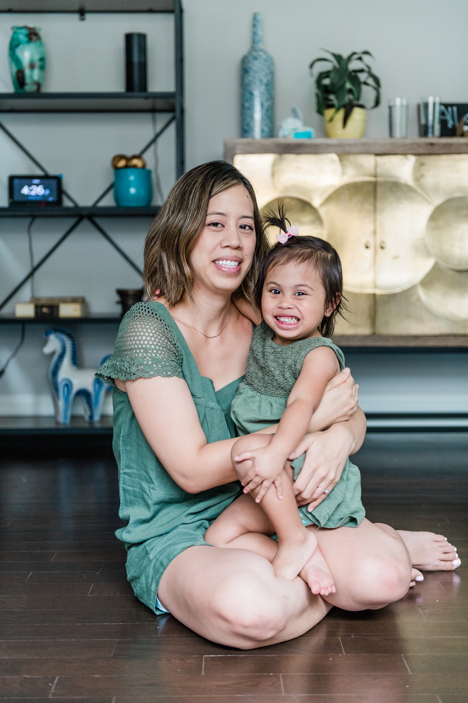 Mother and toddler in green dresses smiling while sitting together on living room floor